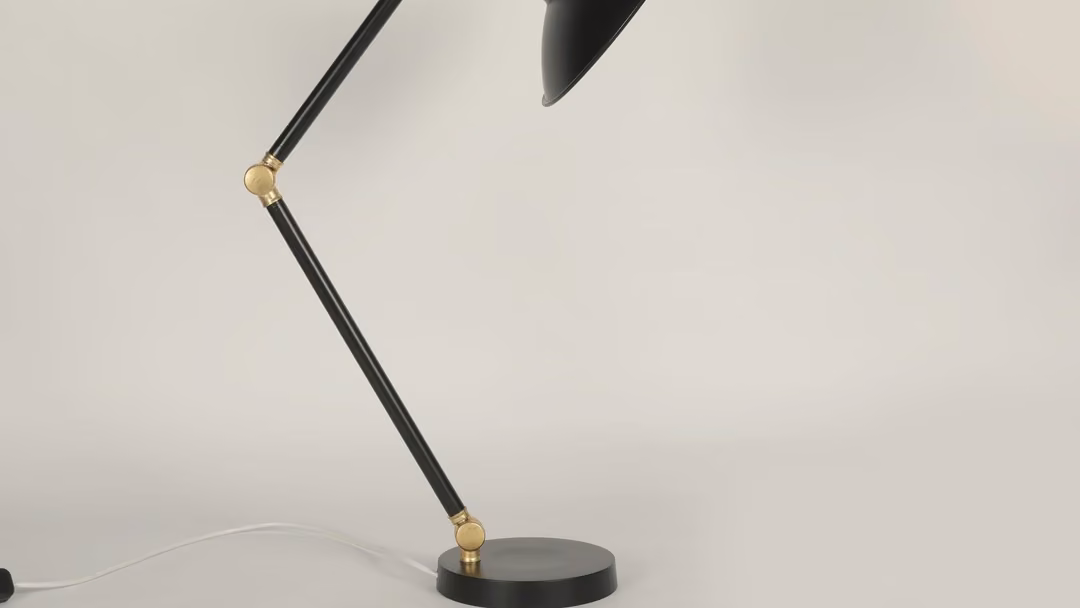 Black-and-brass architect desk lamp against a white wall