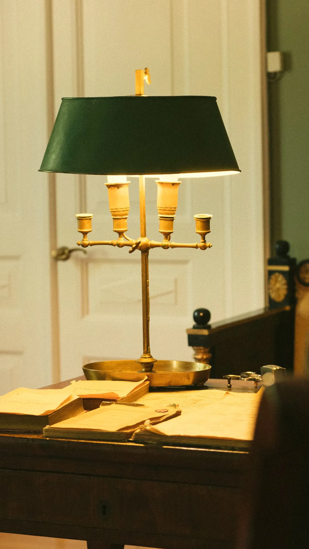 Brass bouillotte lamp with a green shade over a writing desk with old papers