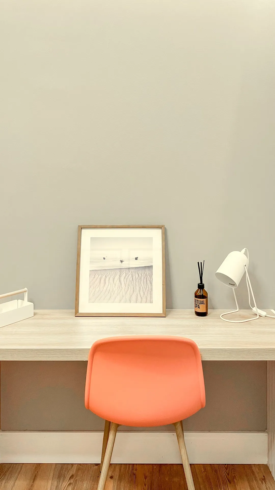 Small white desk lamp on a narrow white desk with a framed print and a coral chair