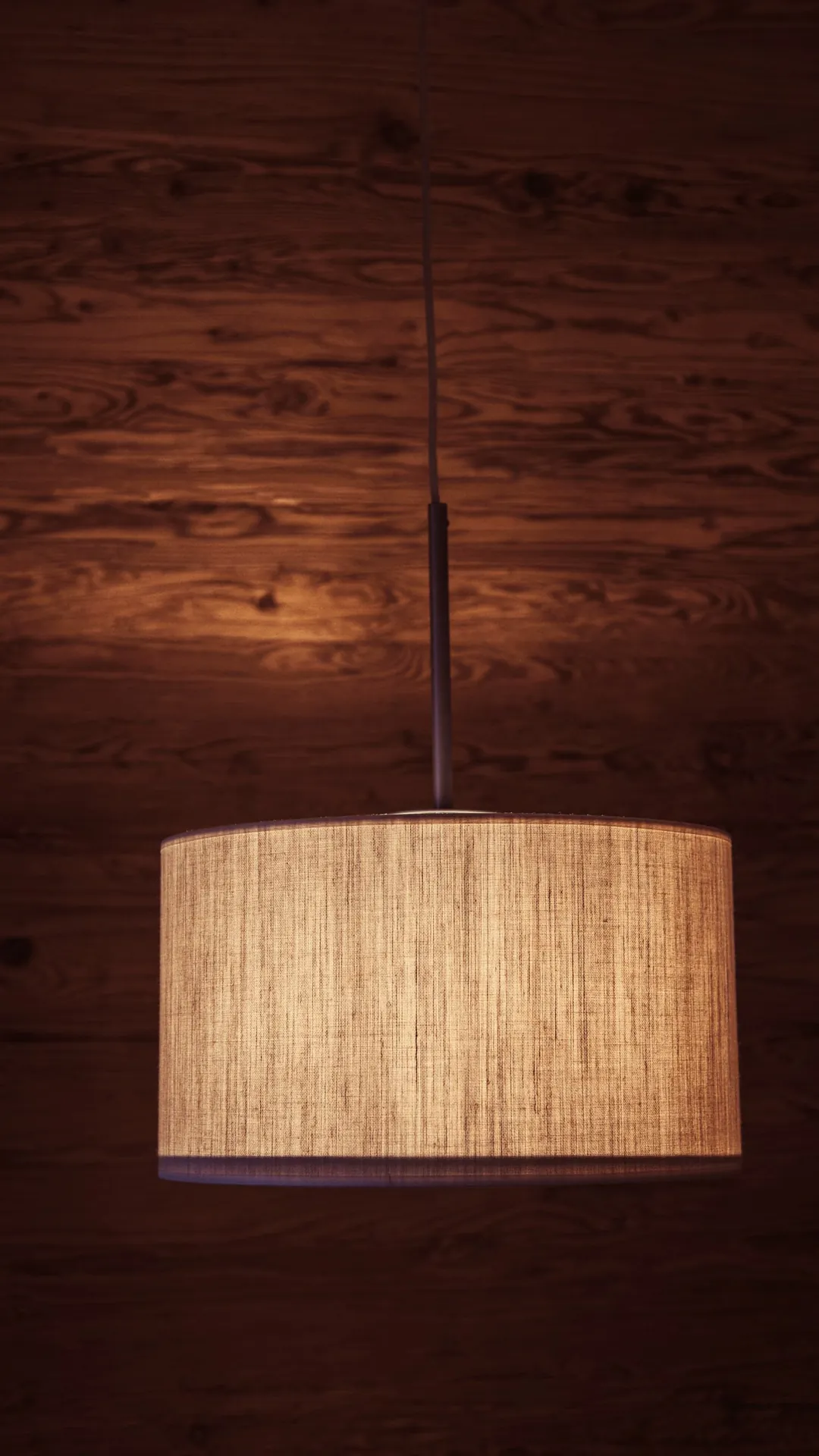 Woven drum pendant shade glowing against a dark wood wall
