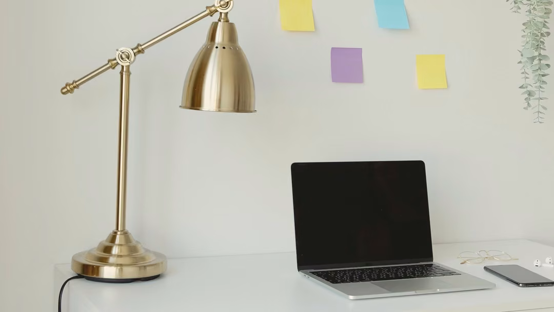 White home-office desk with a brass arm lamp, a laptop, and sticky notes on the wall