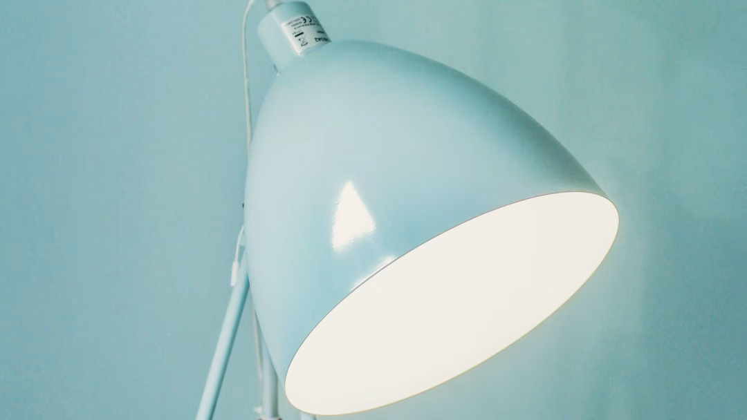 Teal dome desk lamp with its light on, against a teal wall