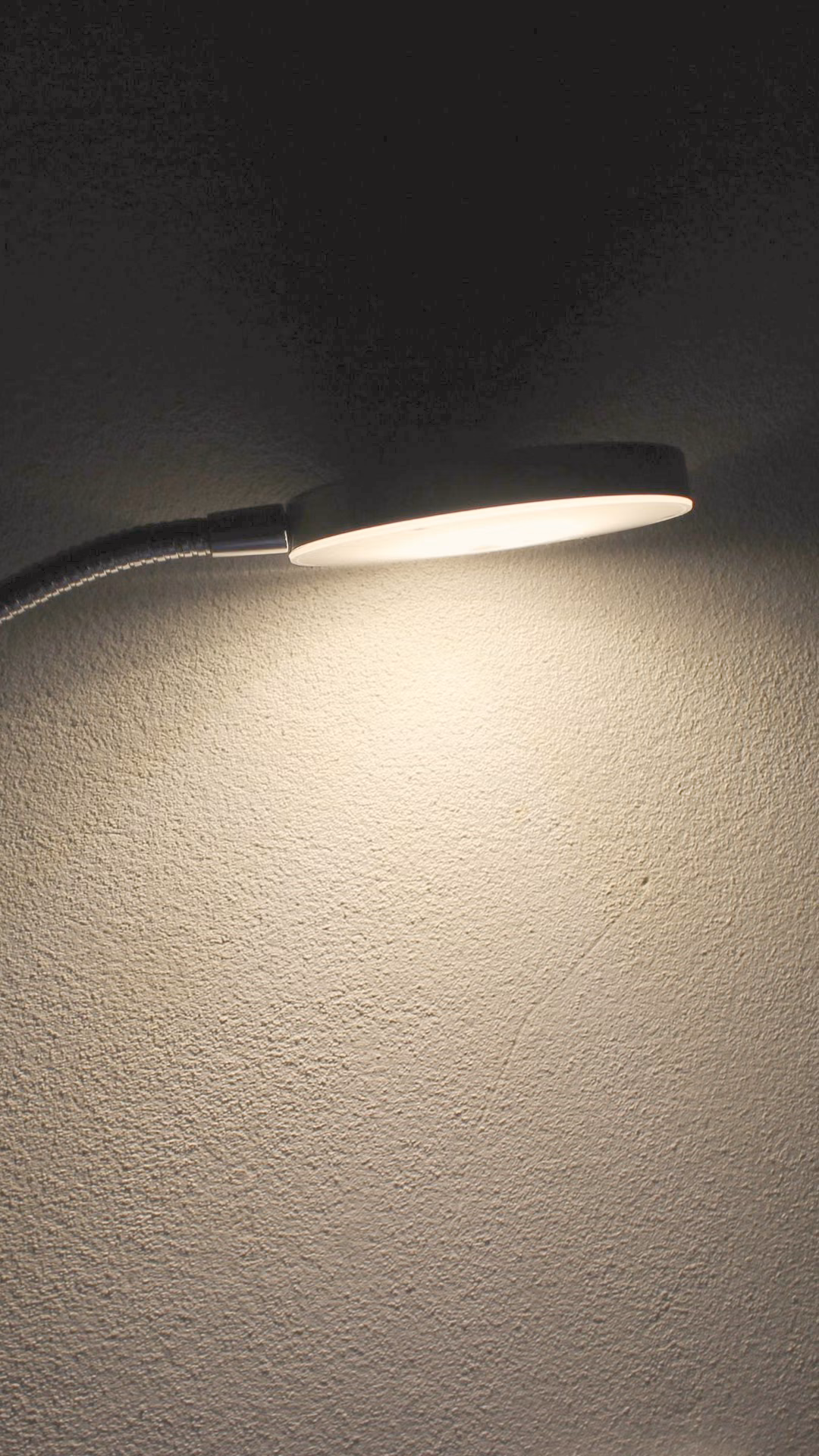 Slim LED disc lamp on a gooseneck casting light on a wall