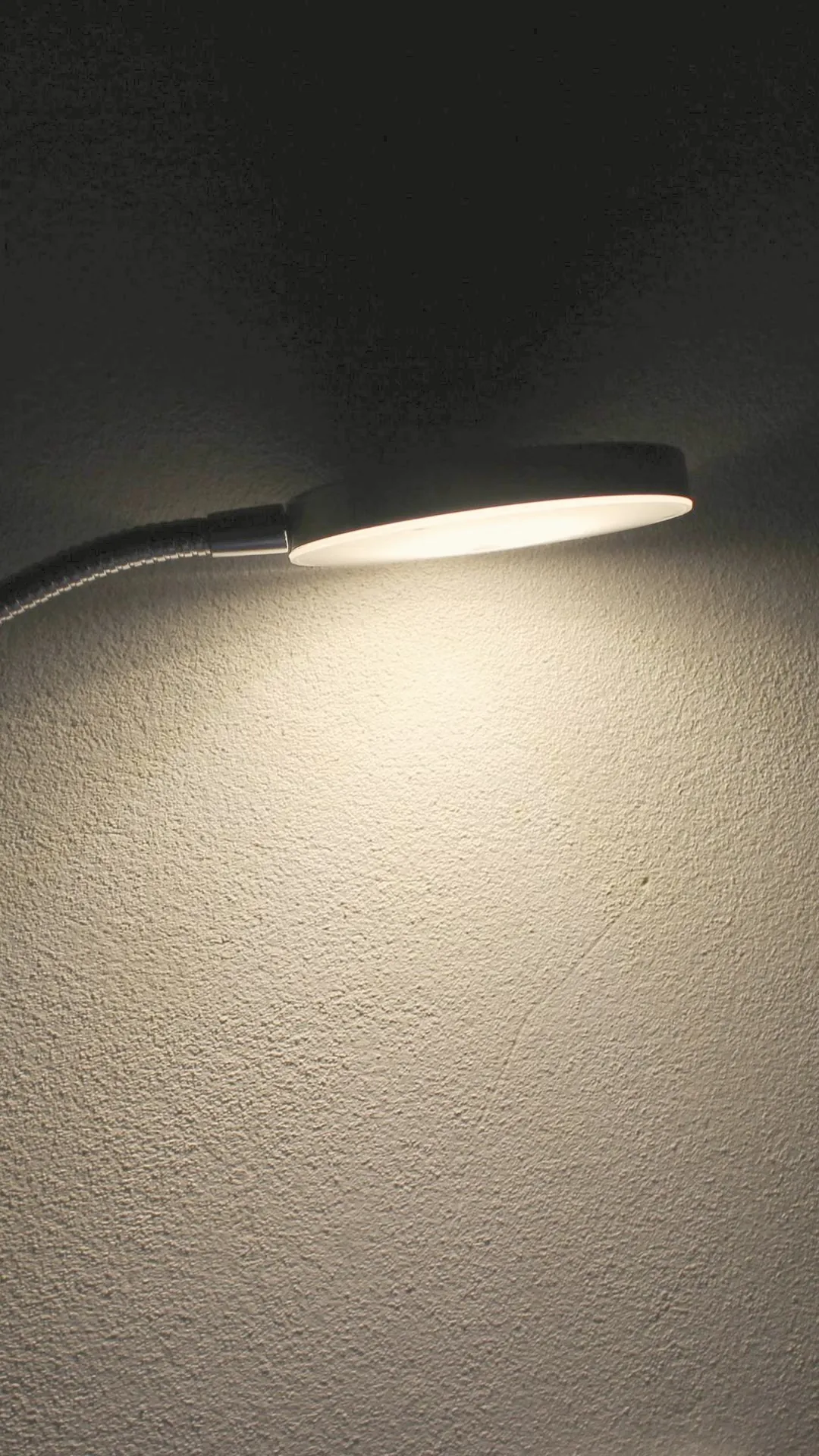 Slim LED disc lamp on a gooseneck casting light on a wall