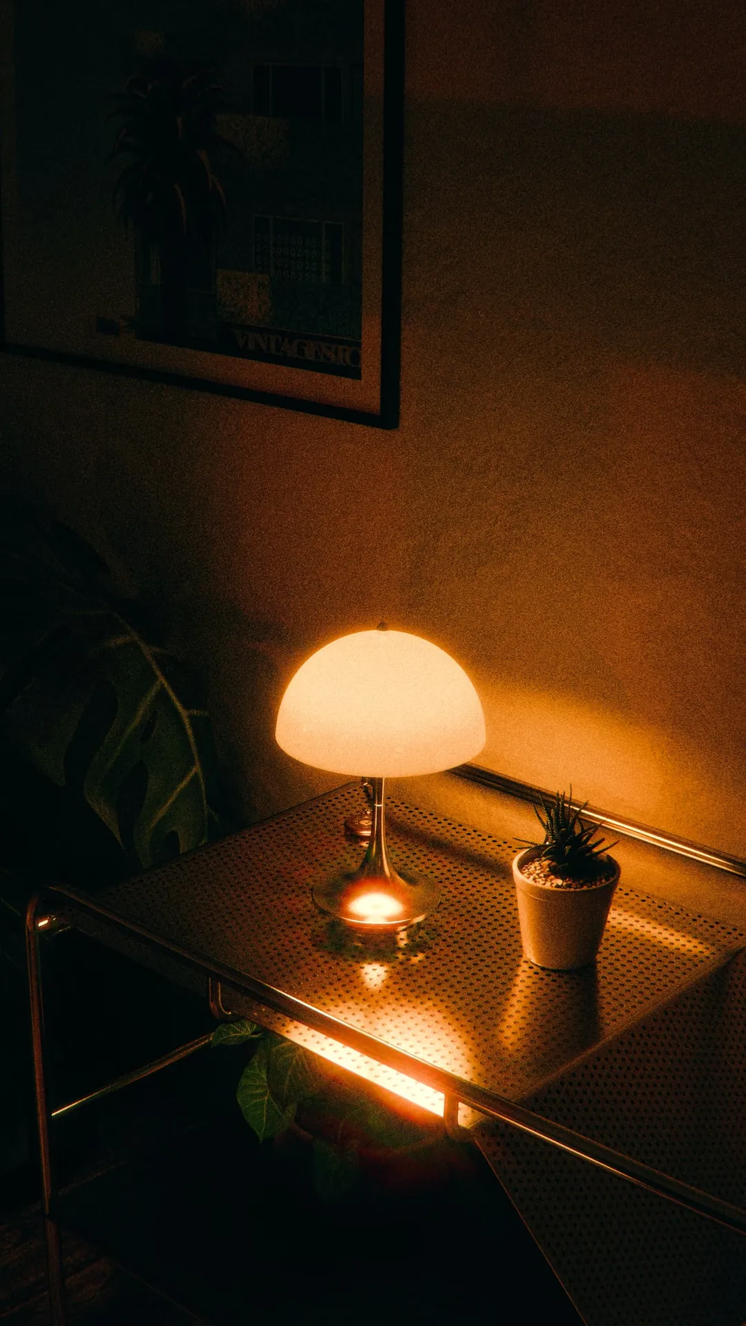 Mushroom lamp casting a warm pool of light on a dark desk beside a small plant