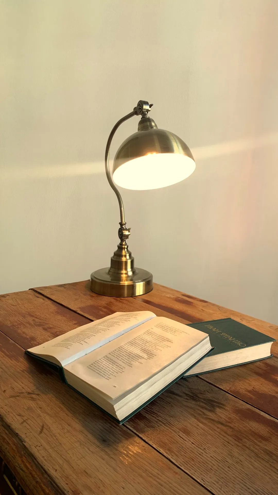 Brass desk lamp with a dome shade lighting an open book on a wooden desk