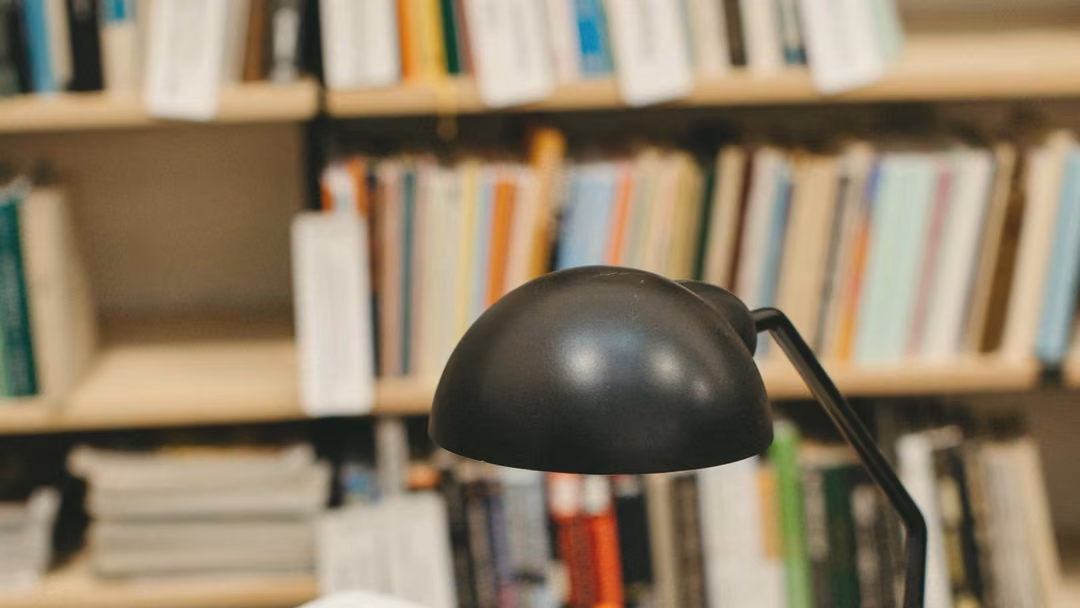 Black desk lamp over drawings on a drafting desk, with bookshelves behind